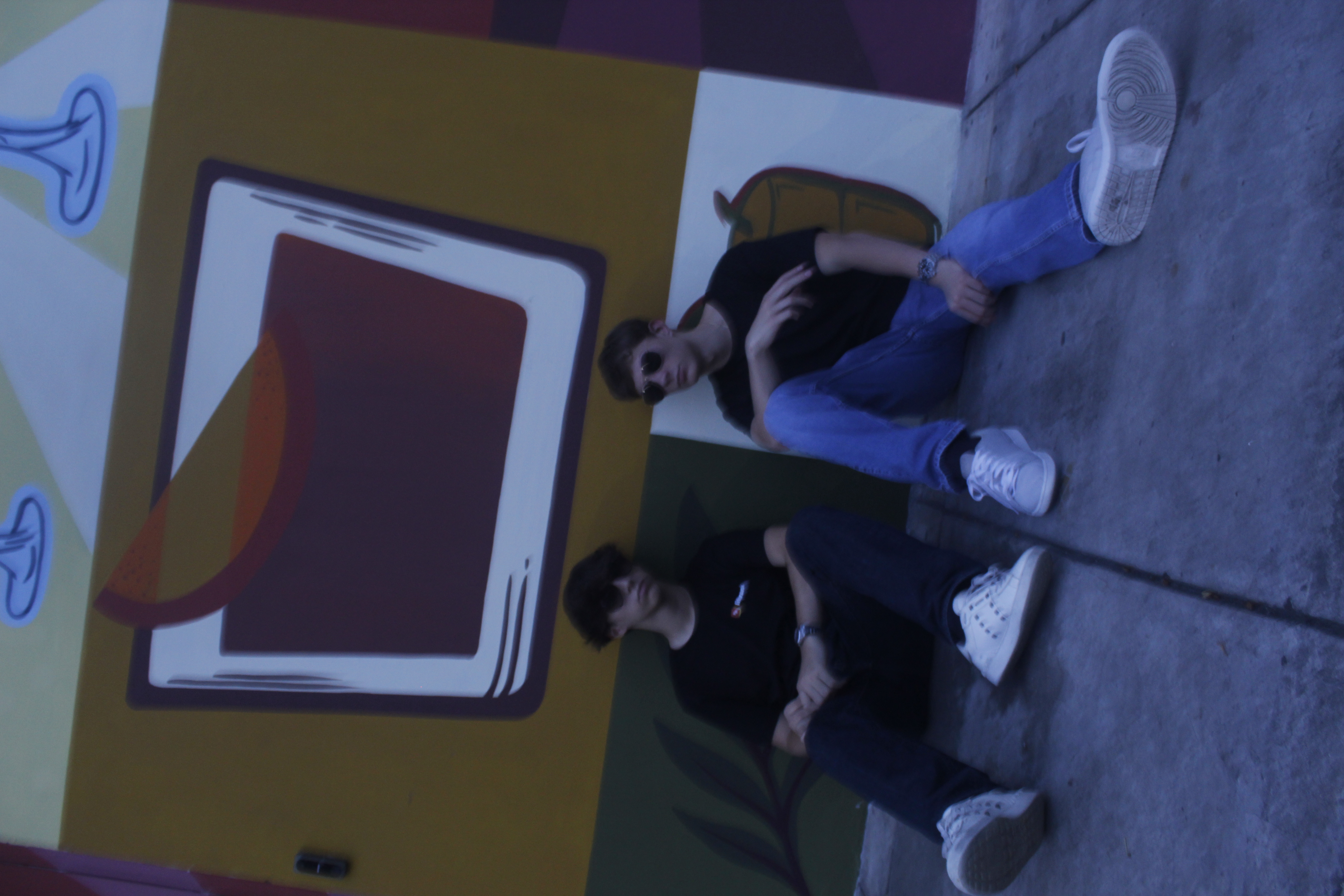 Two people wearing black Liftrank T-shirts while seated in front of a colorful mural